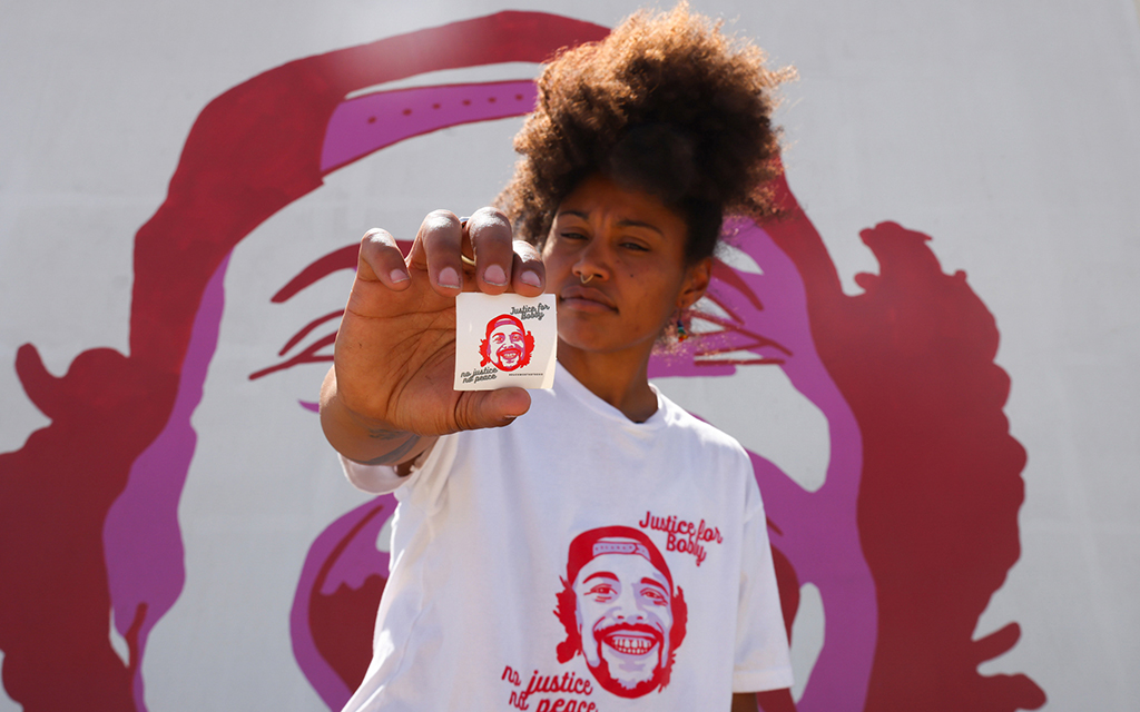 Rae Duckworth holds a “Justice for Bobby” sticker on July 2, 2022, near murals in Salt Lake City remembering the victims of police shootings. After her cousin, Bobby Duckworth, was killed during a mental health call in 2019, Duckworth began passing out these stickers to keep his memory alive. (Photo by Laura Bargfeld/News21)