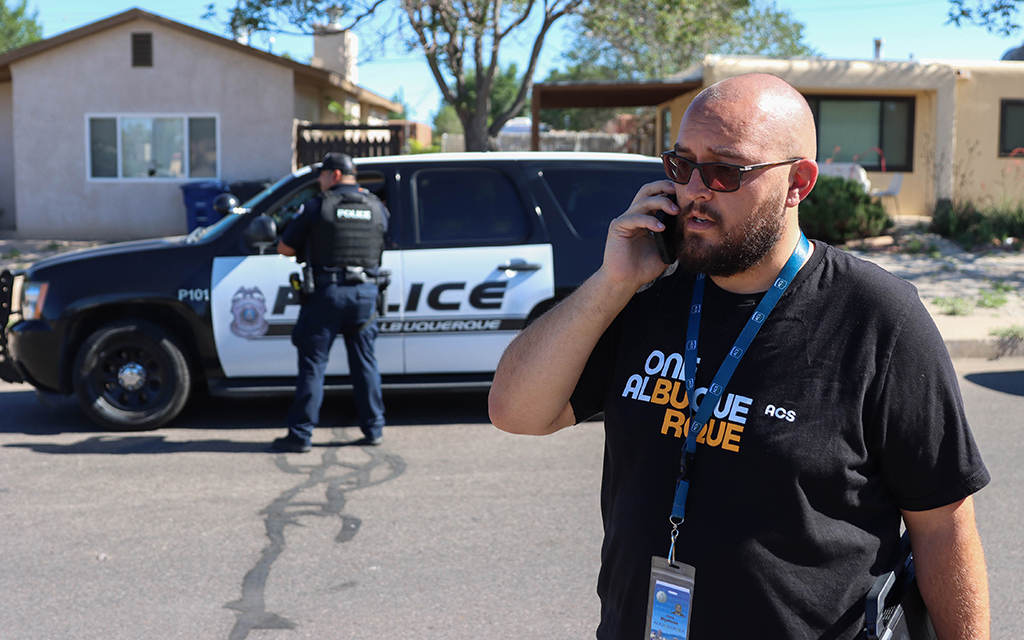 Albuquerque Community Safety responder Chris Blystone makes a phone call while police officers talk on July 7, 2022, in Albuquerque, New Mexico. The new agency responded after a police SWAT raid left a family of five without a home. (Photo by Kate Heston/News21)